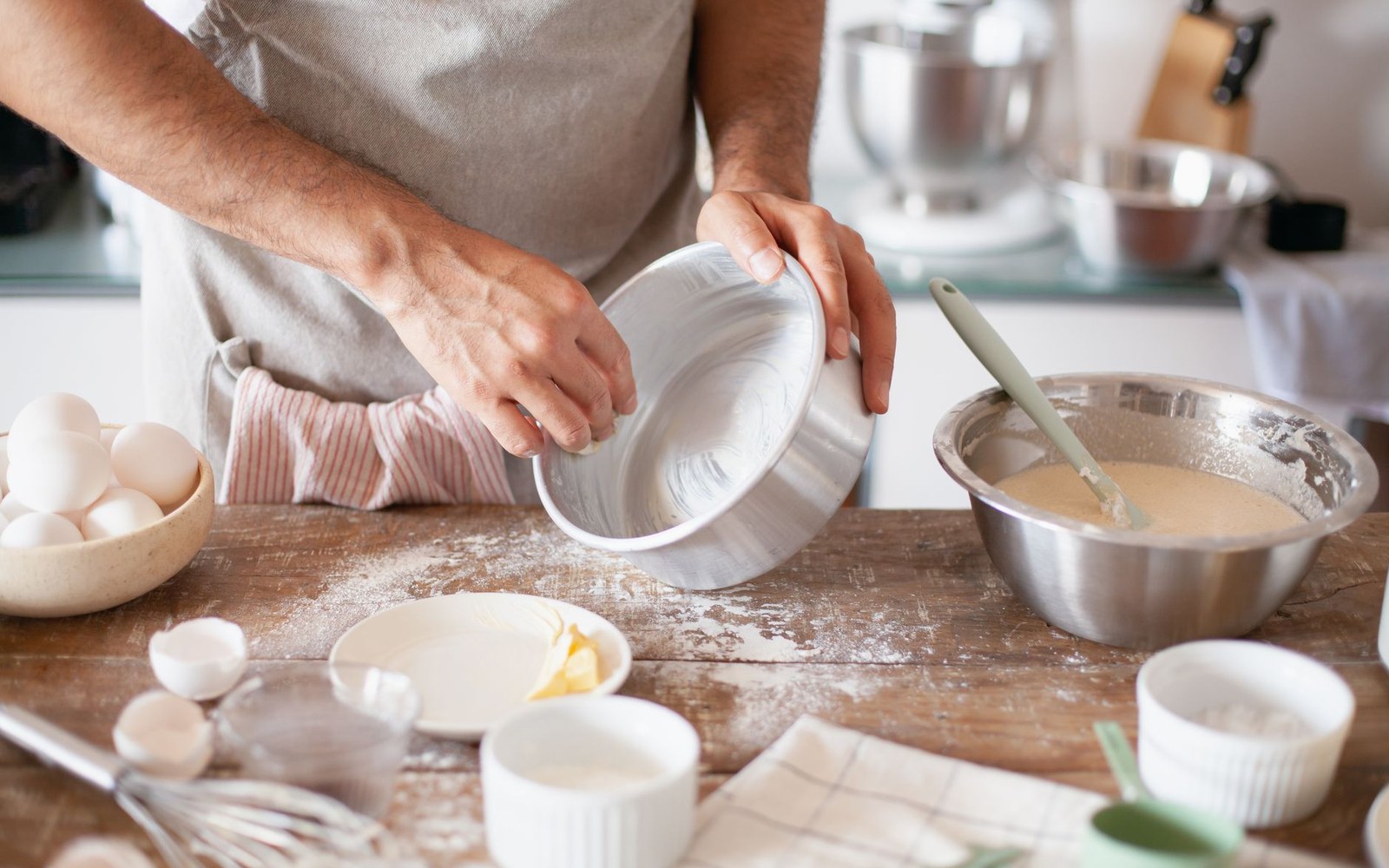 An adult cook working brandy butter in a bowl with a wooden spatula, the butter pale and stiff, a bottle visible behind
