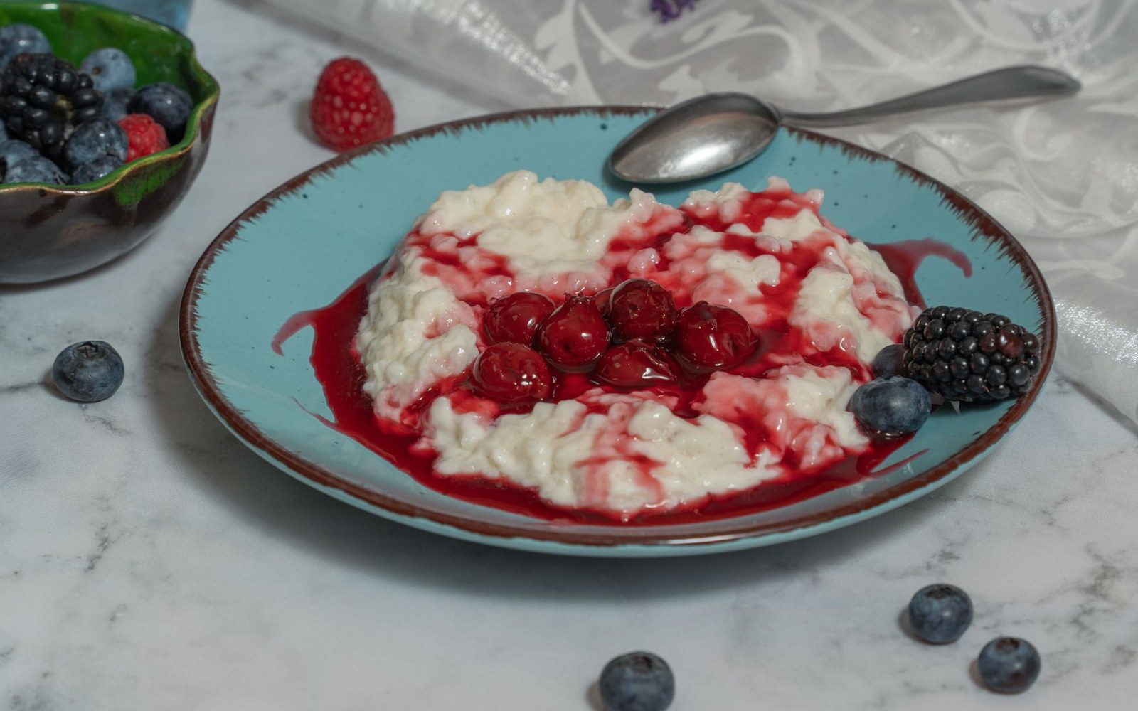 Rice pudding topped with red berry sauce on a blue plate with fresh berries nearby