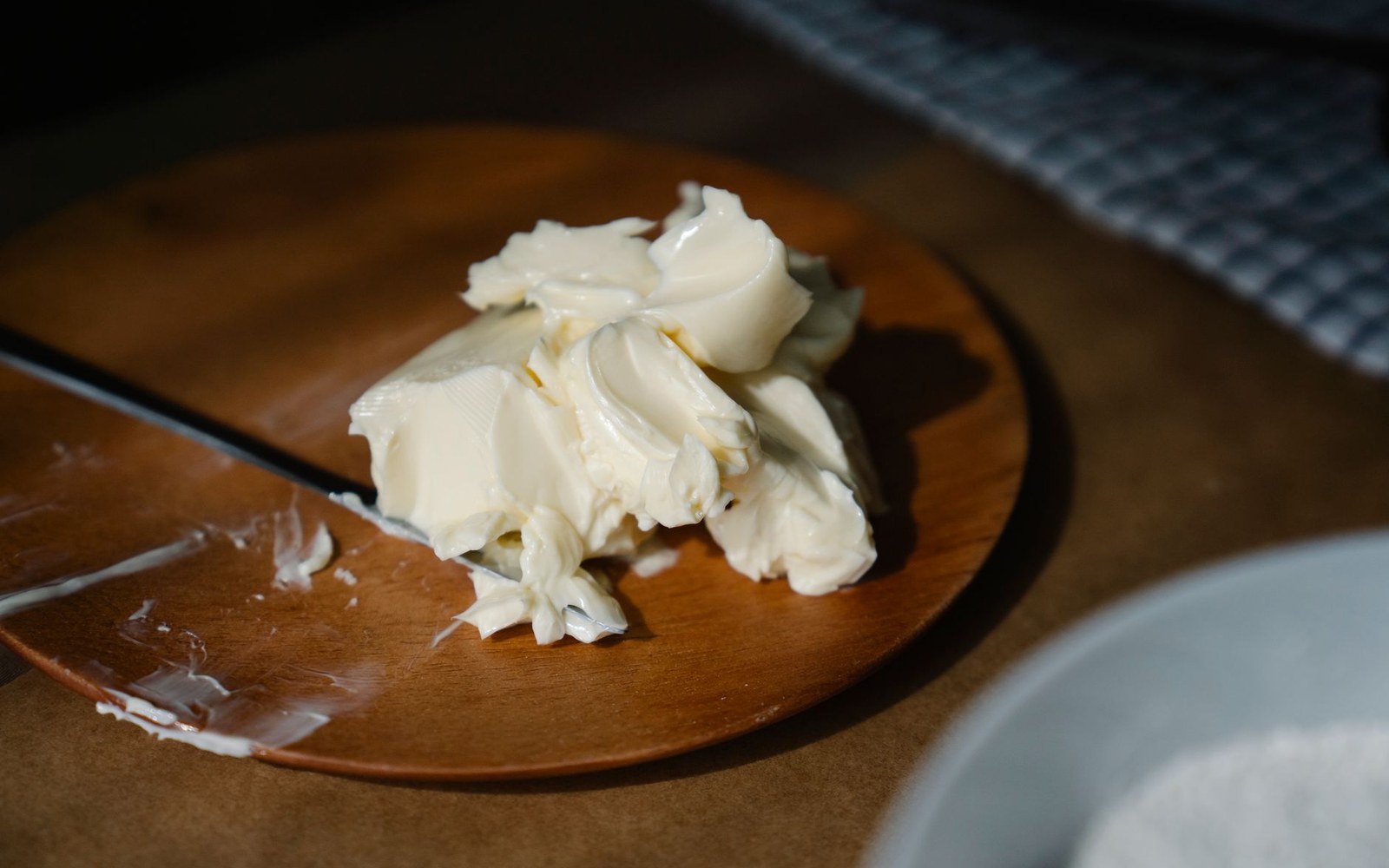 Softened brandy butter piled on a wooden plate beside a knife with residue