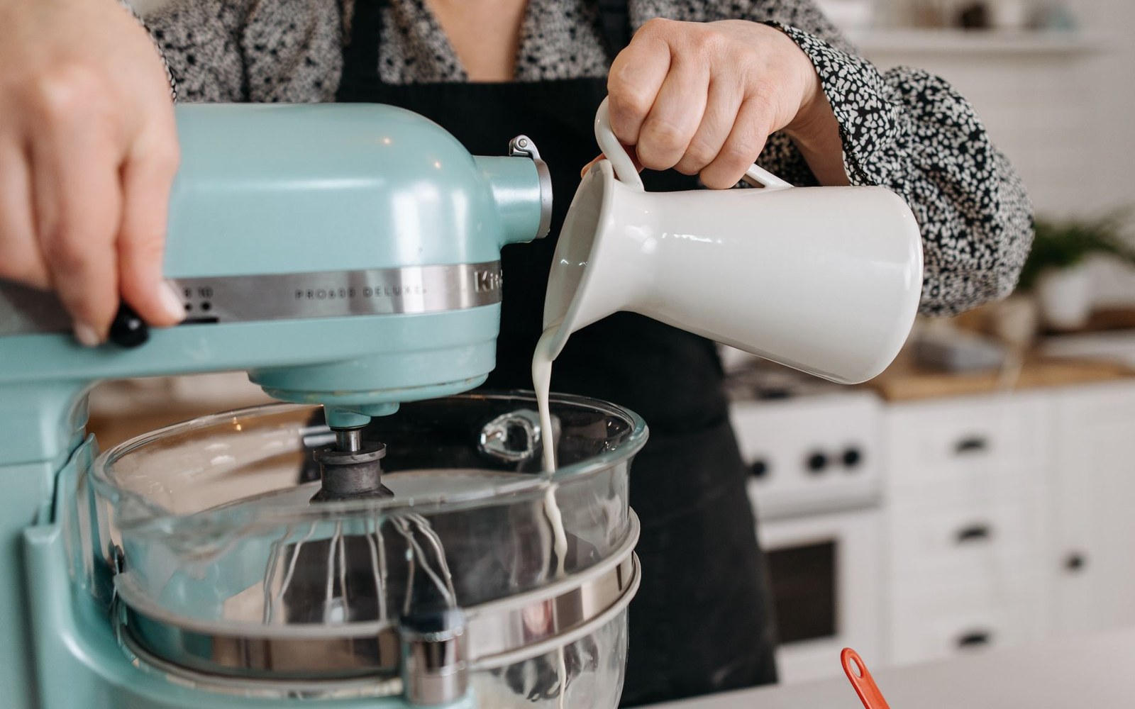 Pouring cream from a jug into a stand mixer's glass bowl