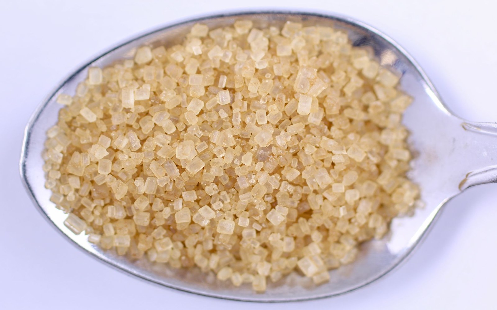 Close-up of coarse brown sugar crystals piled on a metal spoon