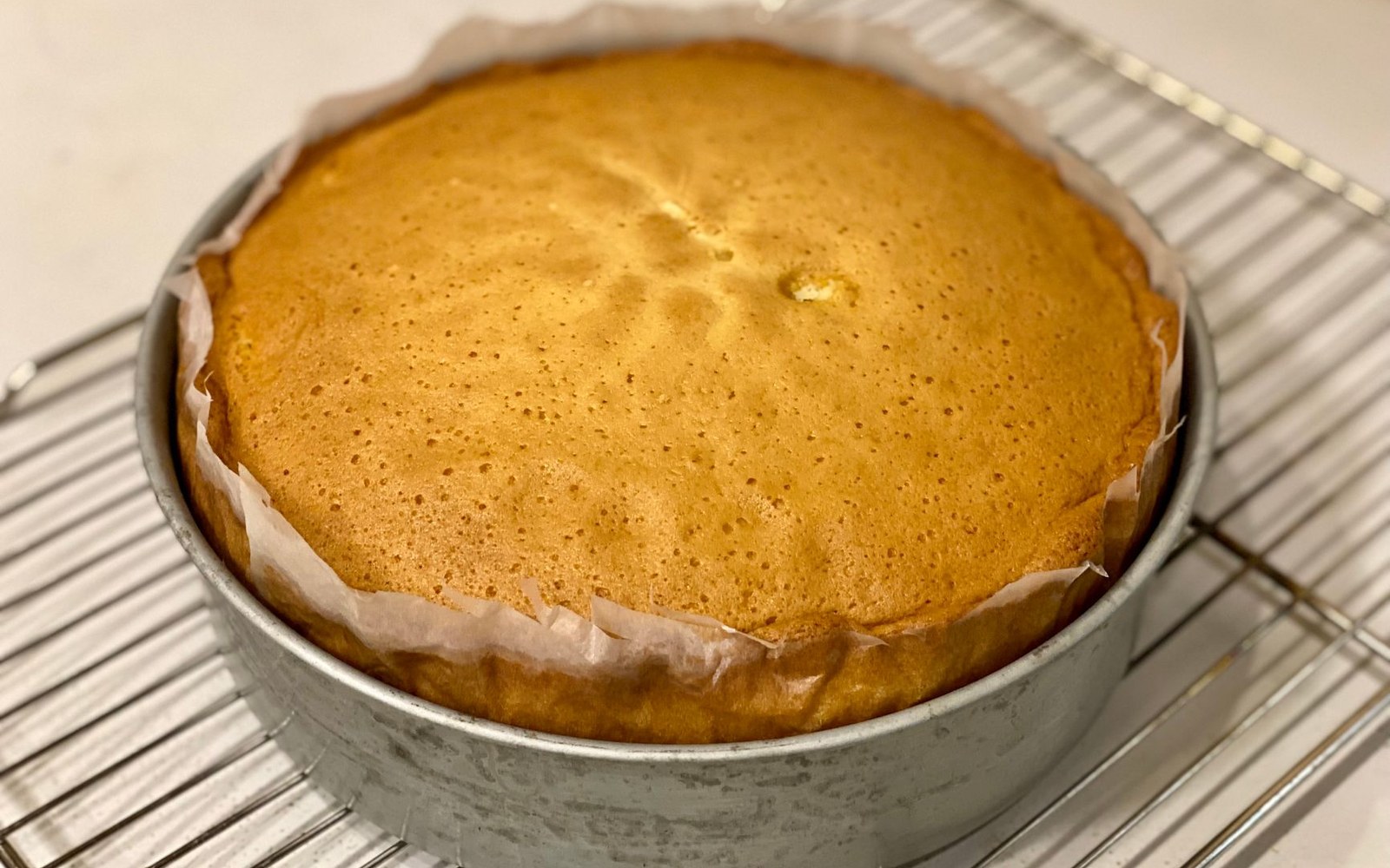 Freshly baked round cake with parchment lining, cooling in its tin on a wire rack