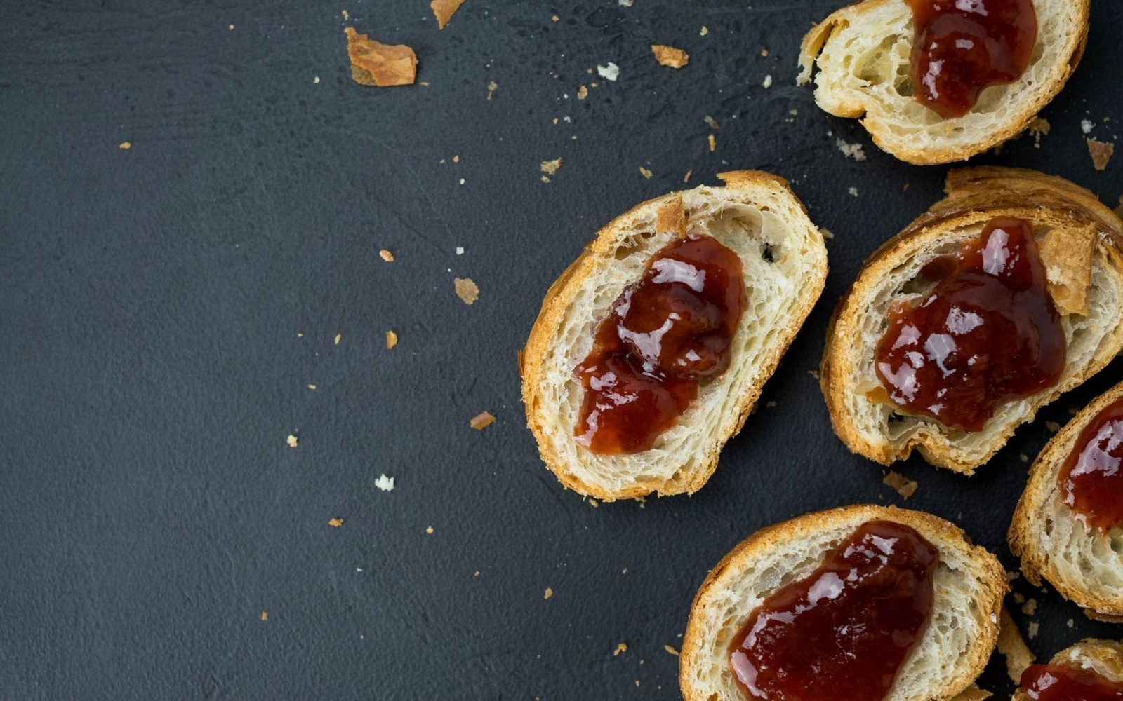 Sliced croissant halves spread with red jam scattered on a dark surface