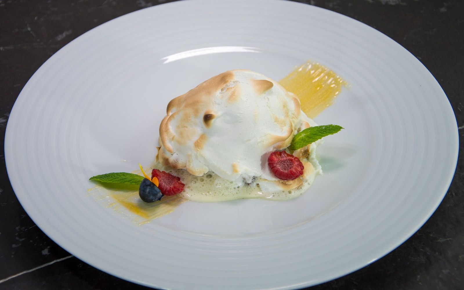 Toasted meringue dessert with custard sauce, berries, and mint on a white plate