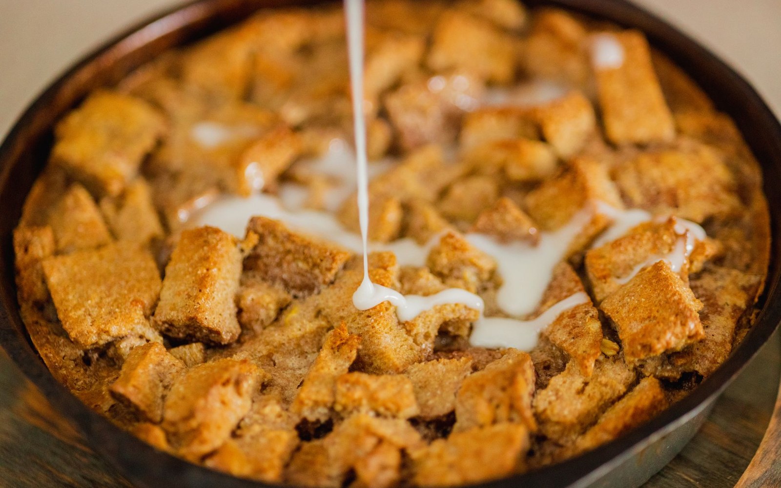 White rum sauce being drizzled over baked bread pudding in a round dish