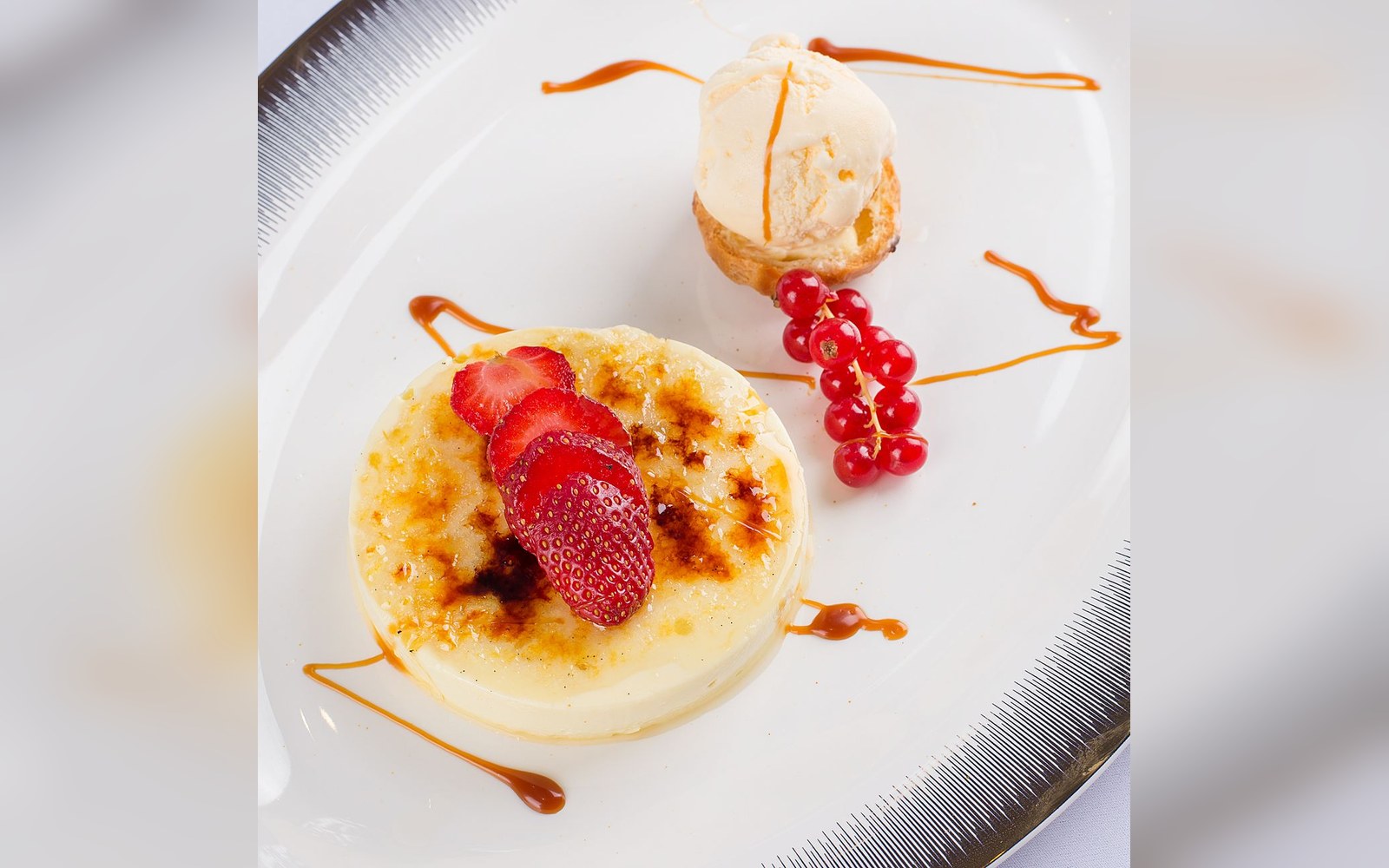 Crème brûlée topped with sliced strawberries, served with redcurrants and vanilla ice cream on a choux pastry