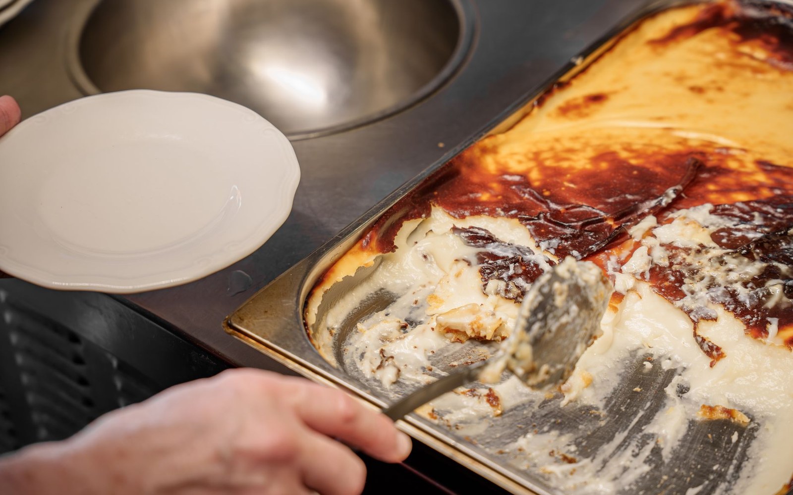 A hand serves sticky toffee pudding from a baking tray onto an empty plate