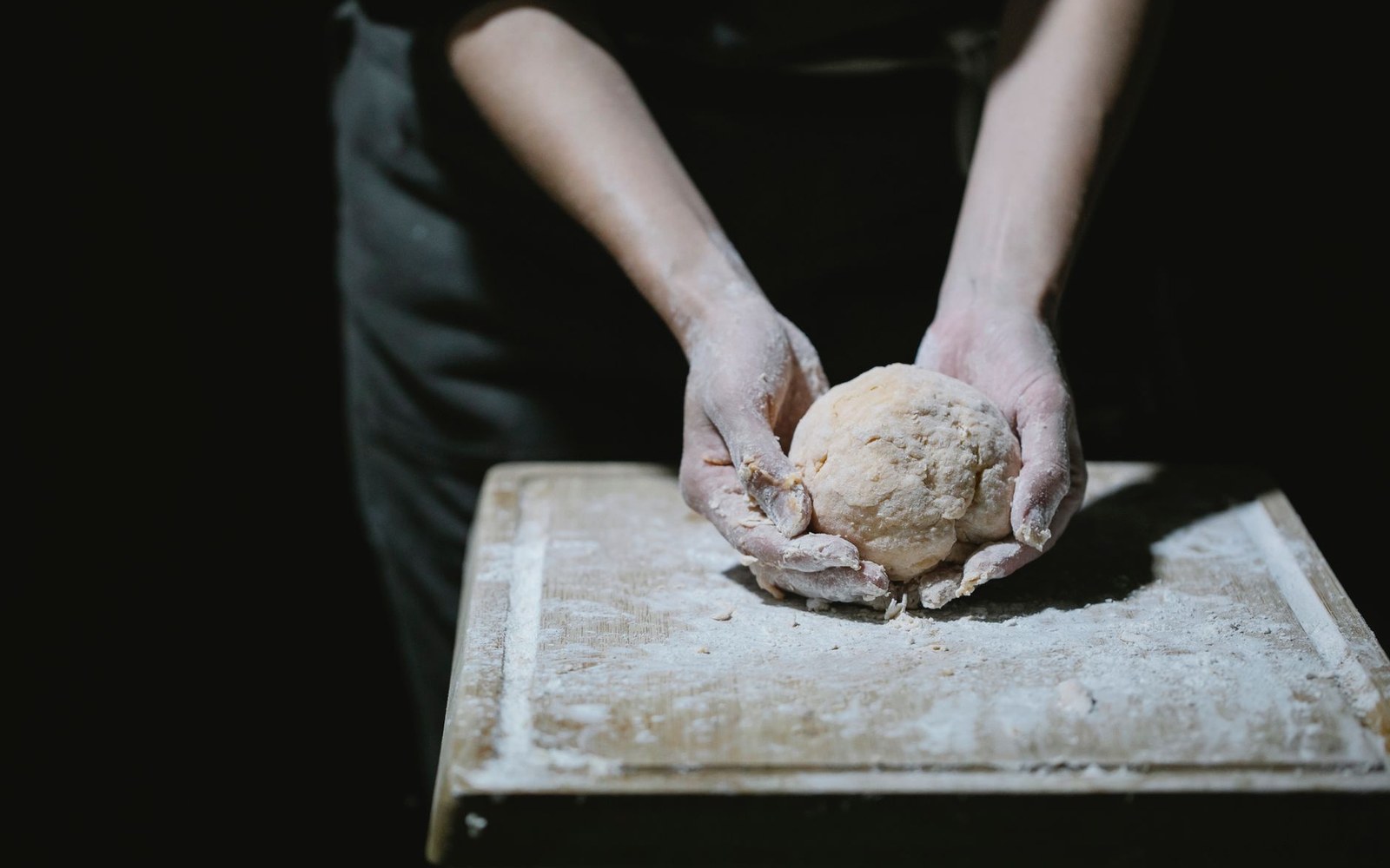 Hands shaping a ball of dough on a flour-dusted wooden board