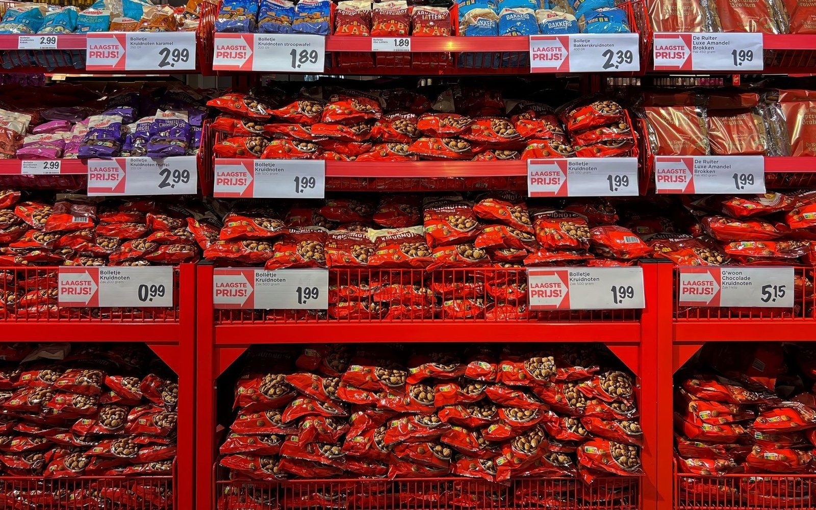 Supermarket shelves stacked with red bags of kruidnoten beneath lowest price tags