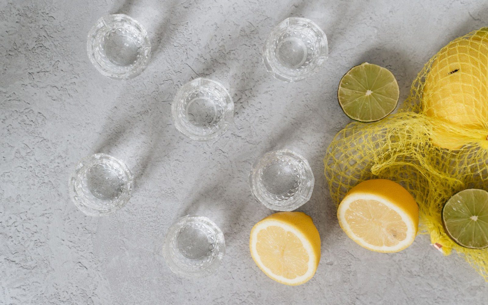 Small crystal glasses arranged beside halved lemons and limes in a mesh bag