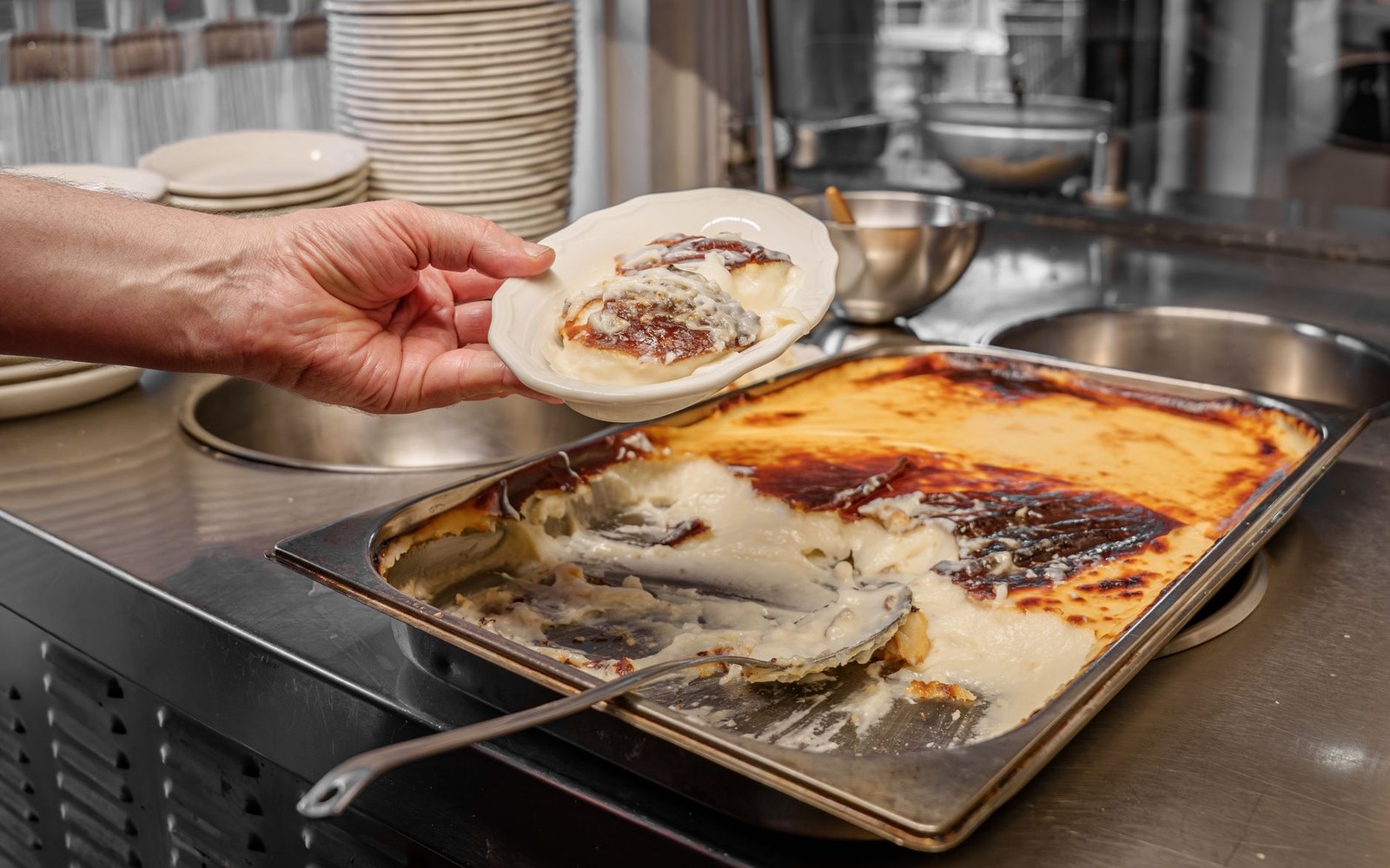 An adult cook's hands holding a ceramic pudding basin just turned out onto a plate, the domed pudding intact, steam rising, dark kitchen background